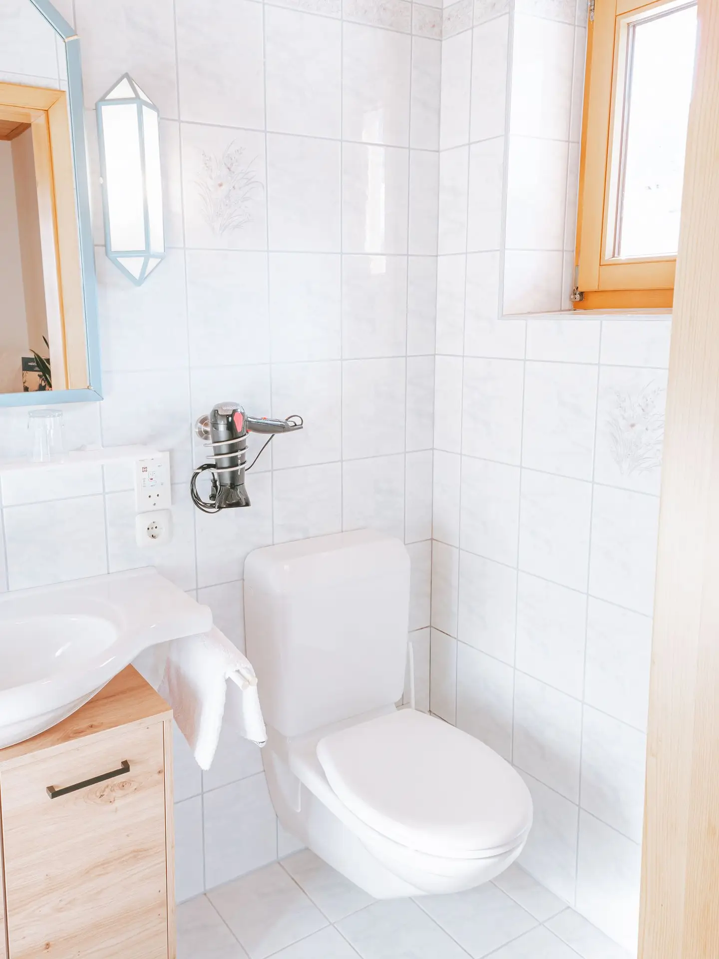 Ein weiß gefliestes Badezimmer mit Toilette und Waschbecken, perfekt für einen erholsamen Urlaub im Salzkammergut in Österreich.