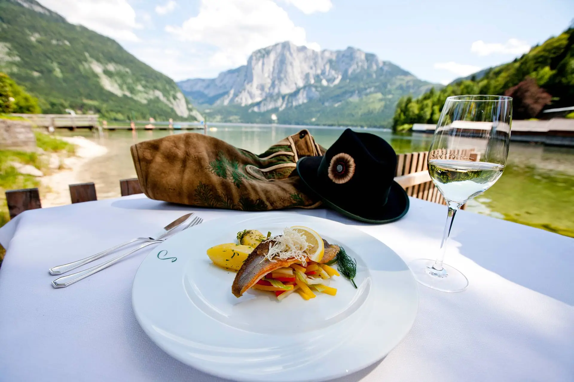 Ein Teller mit Essen und ein Glas Wein auf einem Tisch vor einem Berg im Salzkammergut.